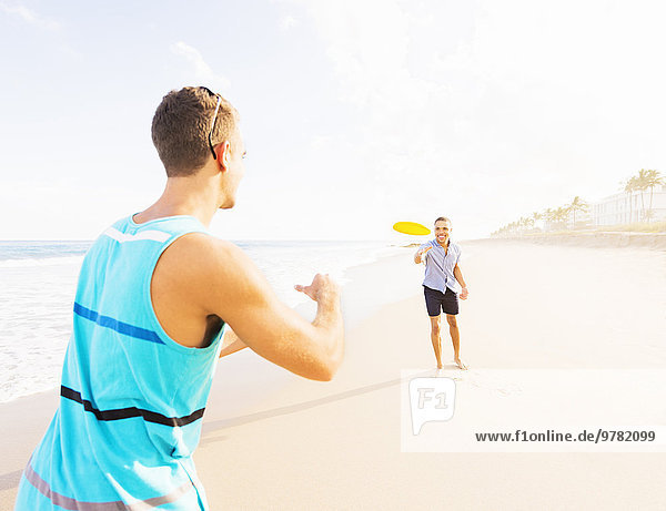 Young men playing plastic disc on beach