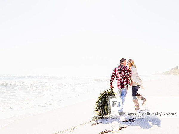 Loving couple walking on beach with tree