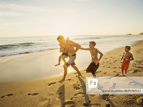 Father playing football on beach with his three sons (6-7  10-11  14-15)