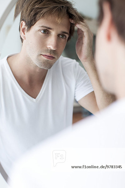 Mann mit zurückweichendem Haaransatz schaut sich selbst im Spiegel an