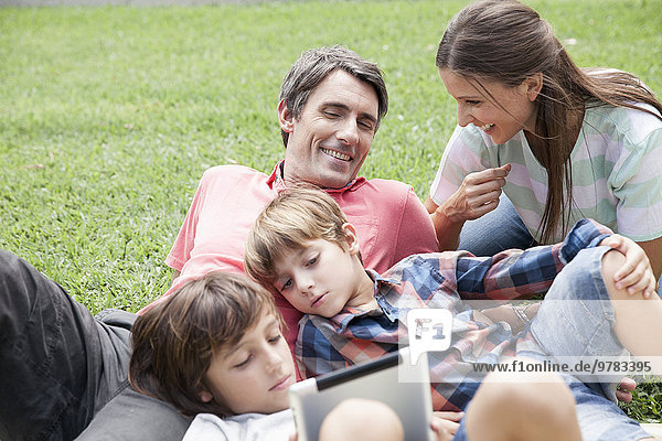 Familie mit zwei Kindern,  die den Nachmittag im Park verbringen,  kleine Jungen,  die ein digitales Tablett benutzen.