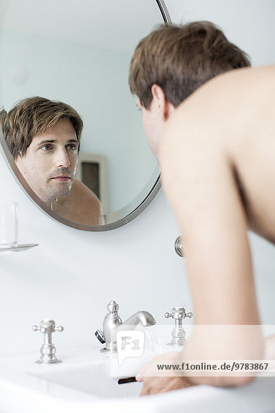 Mann waschen Gesicht im Badezimmer Waschbecken Blick auf sich selbst im Spiegel