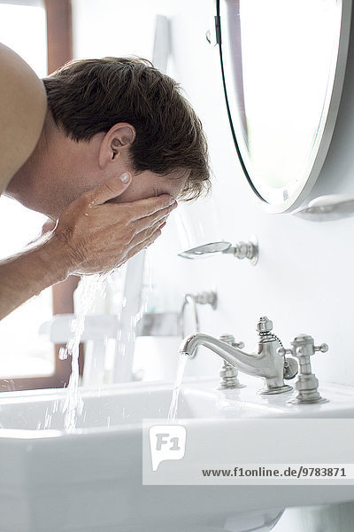 Mann wäscht Gesicht im Badezimmer Waschbecken