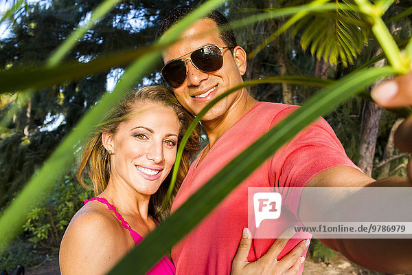 Smiling couple hugging behind palm frond leaves