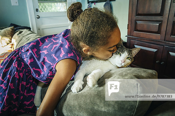 Mixed race girl kissing pet cat on sofa