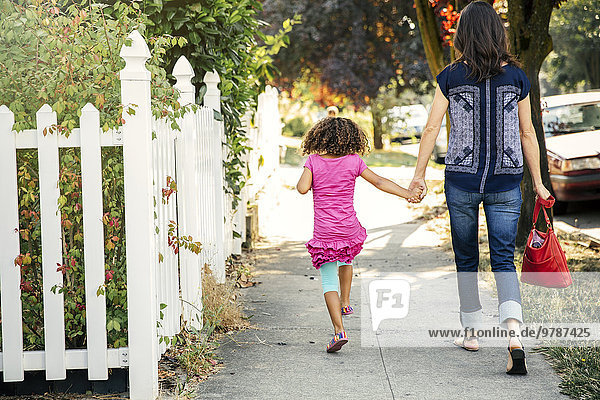Mother and daughter holding hands on sidewalk