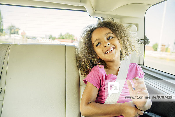 Mixed race girl smiling in back seat of car
