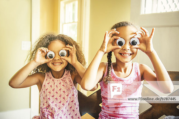 Mixed race sisters playing with googly eyes