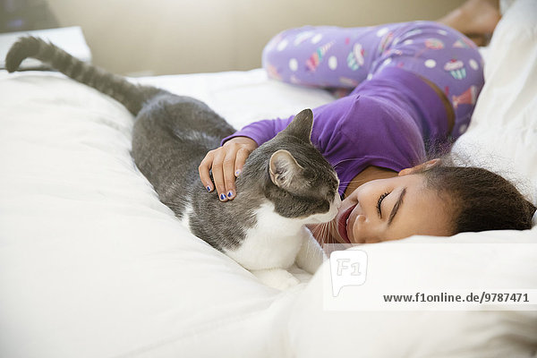 Mixed race girl playing with cat on bed