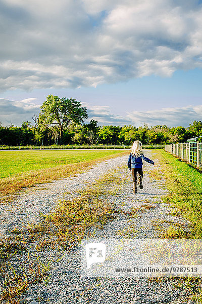 Caucasian girl walking on dirt road on ranch