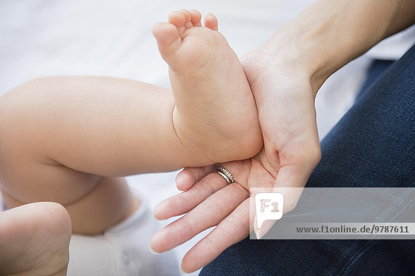 Close up of mixed race mother holding foot of baby