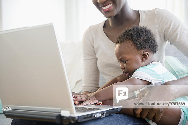Black mother and son using laptop on sofa