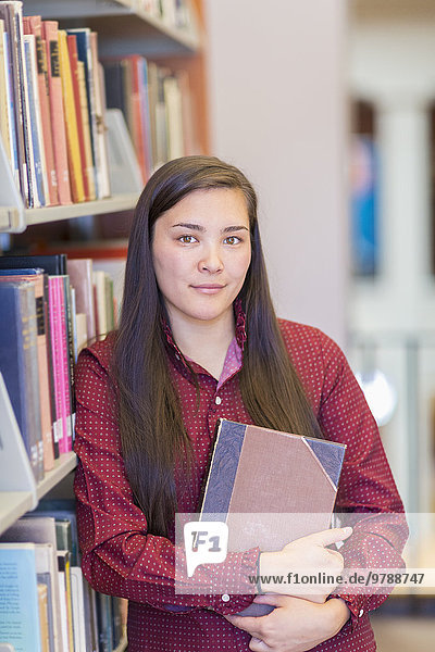 Mixed race student holding book in library