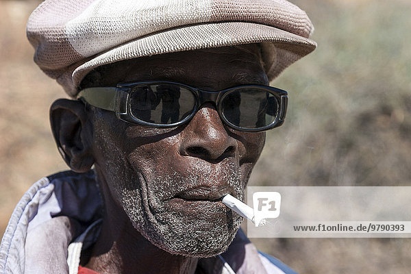 Einheimischer Mann mit Sonnenbrille und Mütze  raucht eine ZigarettePortrait  bei Spitzkoppe  Namibia  Afrika