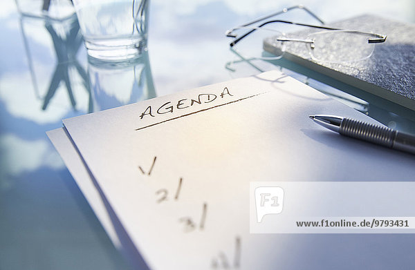 Close up of desk with glass glasses and note saying 'agenda' pen