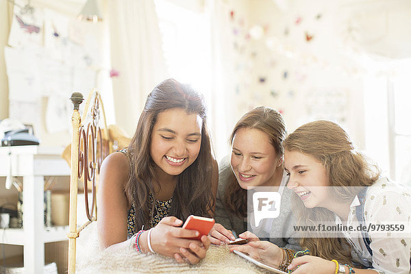 Drei Mädchen im Teenageralter  die zusammen auf dem Bett im Schlafzimmer liegen und ein Smartphone benutzen.