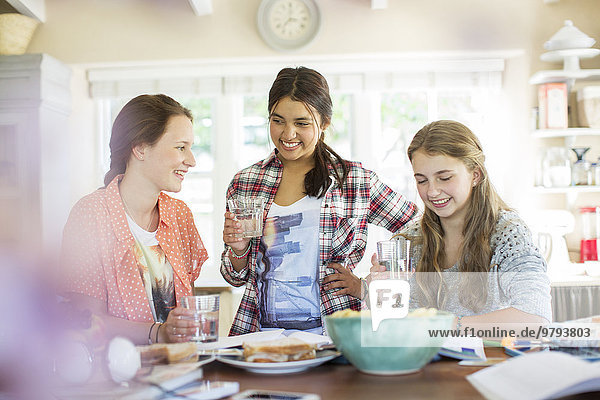 Drei Teenager-Mädchen beim Trinken und Essen am Tisch in der Küche