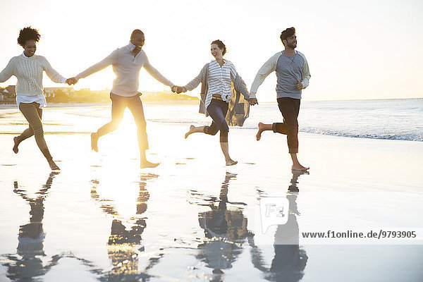 Gruppe von vier Freunden  die Händchen halten und am Strand rennen.