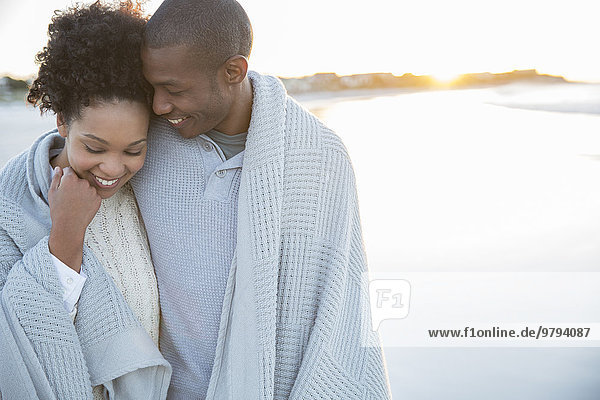 Portrait of couple wrapped in blanket on beach