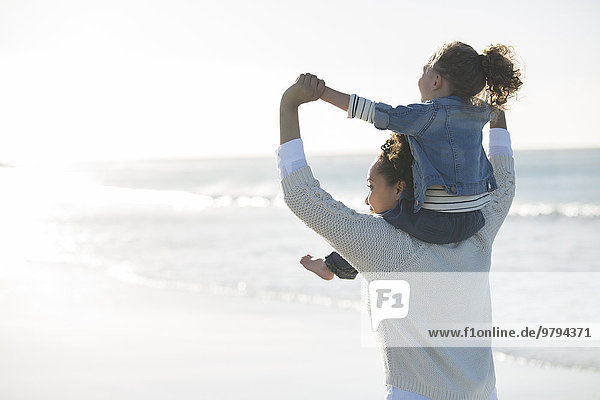 Mother carrying daughter on her shoulders on beach