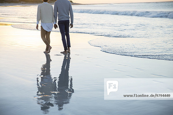Paar hält sich an den Händen und geht am Strand spazieren.