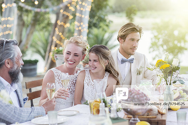 Junges Paar und seine Gäste sitzen bei der Hochzeitsfeier im Garten am Tisch