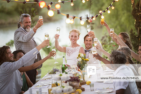 Junges Paar und seine Gäste stoßen bei der Hochzeitsfeier im Garten mit Champagner an.