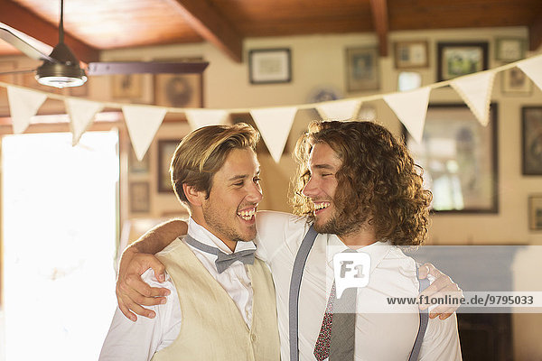 Bridegroom and best man embracing in domestic room