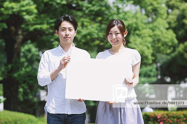 Young smiling Japanese couple holding white board in a park