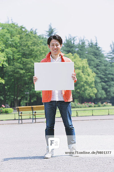 Young smiling Japanese man holding white board in a park