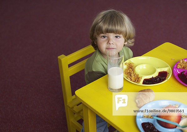 Kind im Kindergarten sitzt vor Frühstücksteller