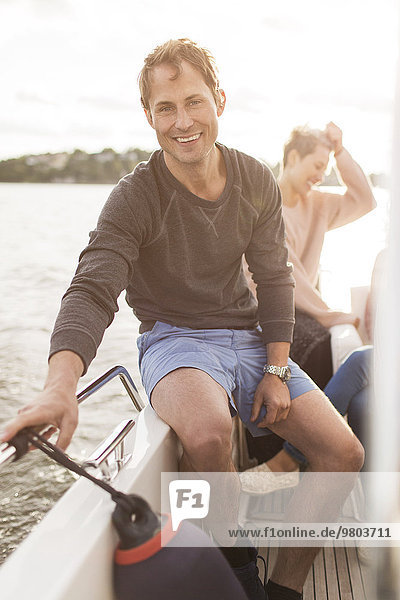 Porträt eines glücklichen Mannes auf der Yacht mit weiblichen Freunden im Hintergrund