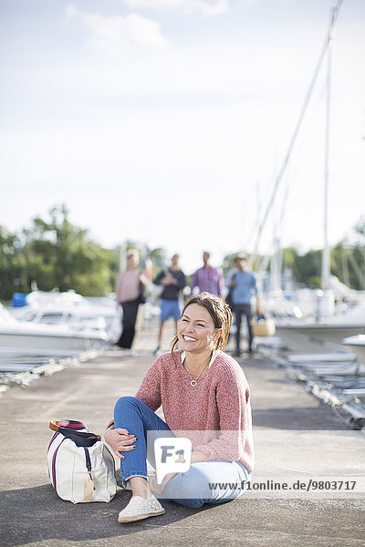 Glückliche Frau sitzt am Pier mit Freunden im Hintergrund