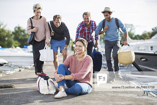 Group of playful friends looking at happy woman on pier at harbor