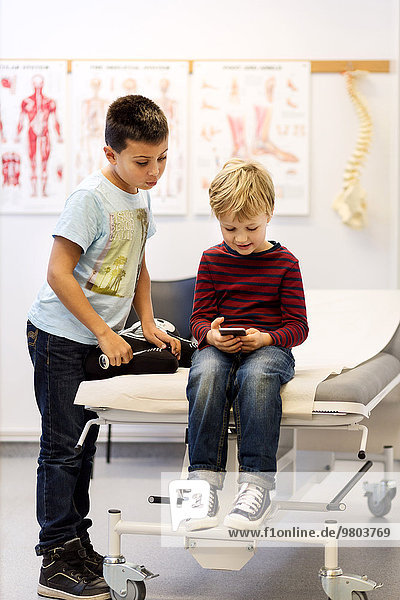 Brüder mit Smartphone am Untersuchungstisch in der orthopädischen Klinik