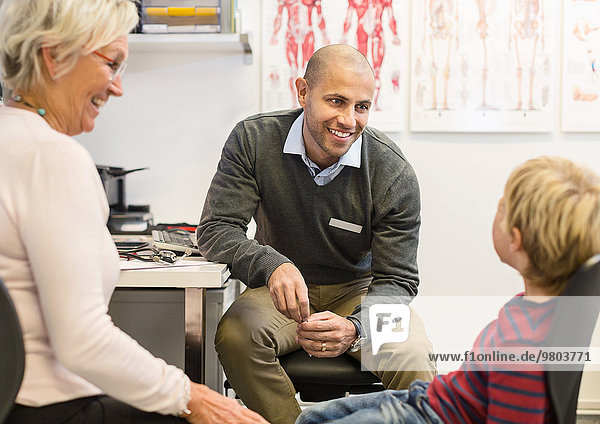 Fröhliche Seniorin beim Blick auf den Enkel im Gespräch mit dem Arzt der Orthopädischen Klinik