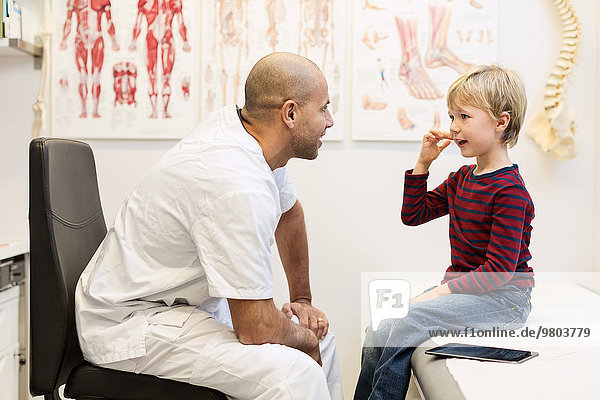 Male orthopedic doctor talking to boy sitting on examination table in clinic