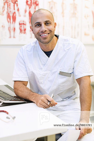 Porträt eines glücklichen orthopädischen Arztes am Schreibtisch in der Klinik