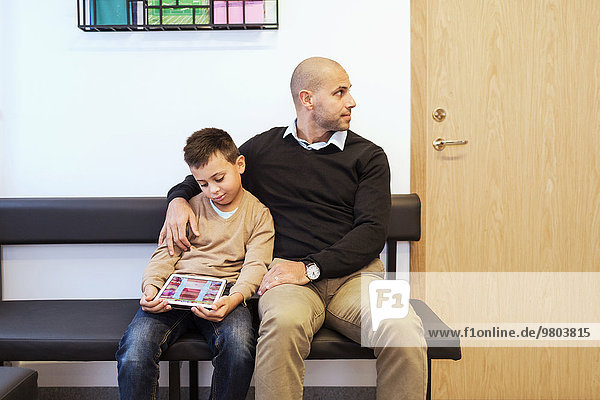 Father and son sitting in waiting room of orthopedic clinic