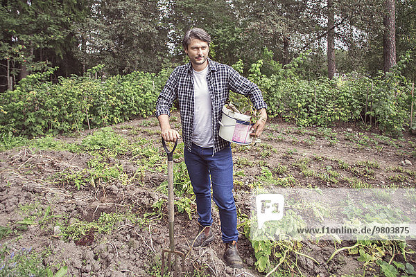 Porträt eines selbstbewussten Mannes mit Gartengabel und Eimer auf dem Biobauernhof.