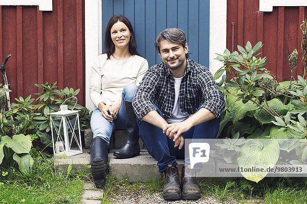 Portrait of smiling mid adult couple sitting outside farmhouse