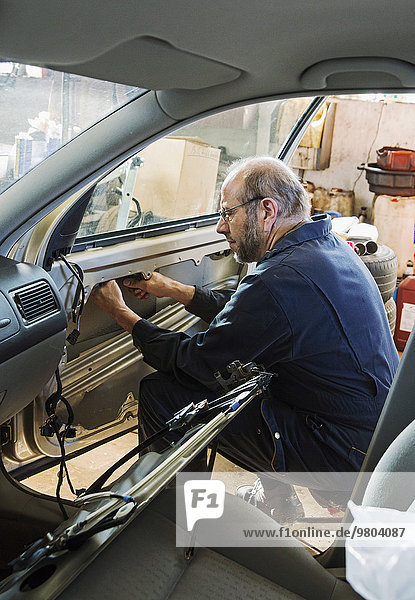 Side view of senior male mechanic fixing car door at garage