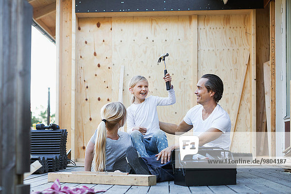 Happy parents with daughter holding hammer while sitting outside house