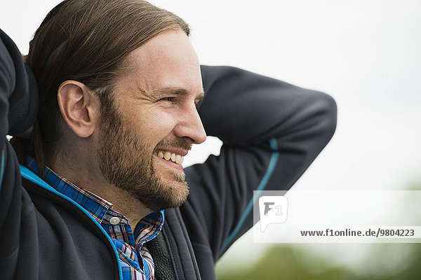 Happy man with hands behind head looking away outdoors