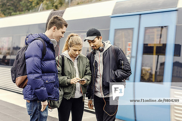 Multiethnische Universitätsstudenten mit dem Handy an der U-Bahn-Station