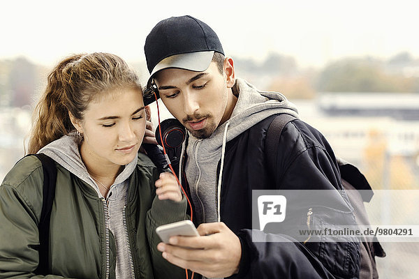Young couple listening music through mobile phone outdoors