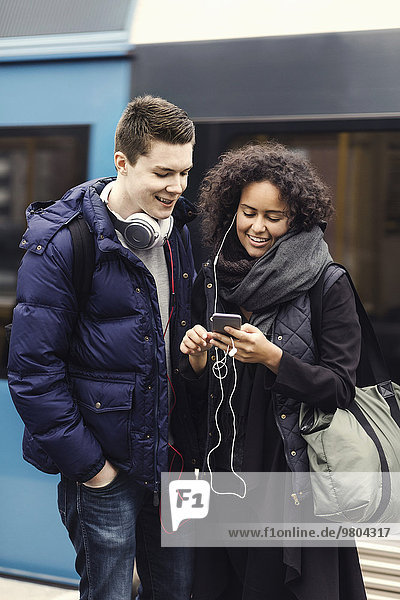 Multi-ethnisches Paar  das Musik über Handy auf der U-Bahn-Plattform hört.