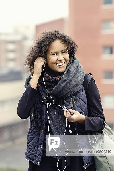 Porträt einer glücklichen Studentin in warmer Kleidung mit Kopfhörern im Freien