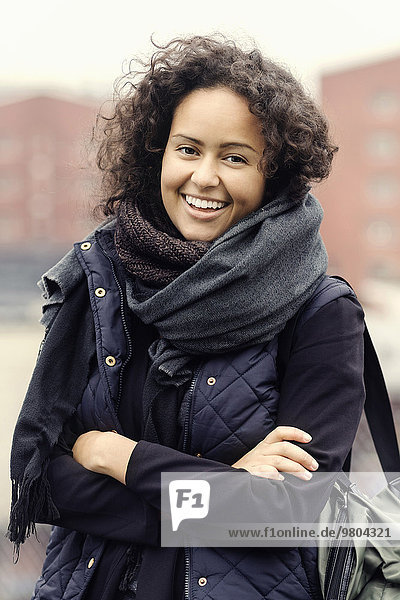 Porträt einer glücklichen Studentin in warmer Kleidung mit gekreuzten Armen im Freien