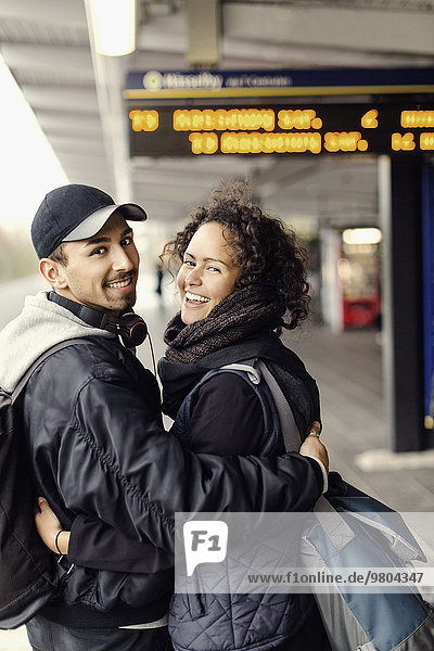 Side view portrait of happy couple with arms around on subway platform